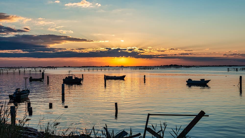 Un coucher de soleil sur une étendue d’eau calme, où plusieurs bateaux sont amarrés.