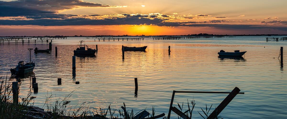 A sunset over a calm water body with several boats anchored.