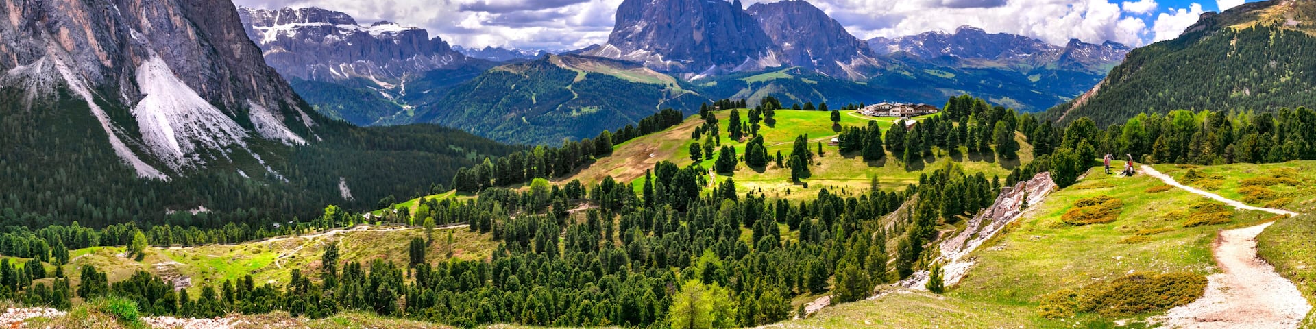 Un paisaje montañoso con cielo despejado, un sendero sinuoso y un edificio en una colina.
