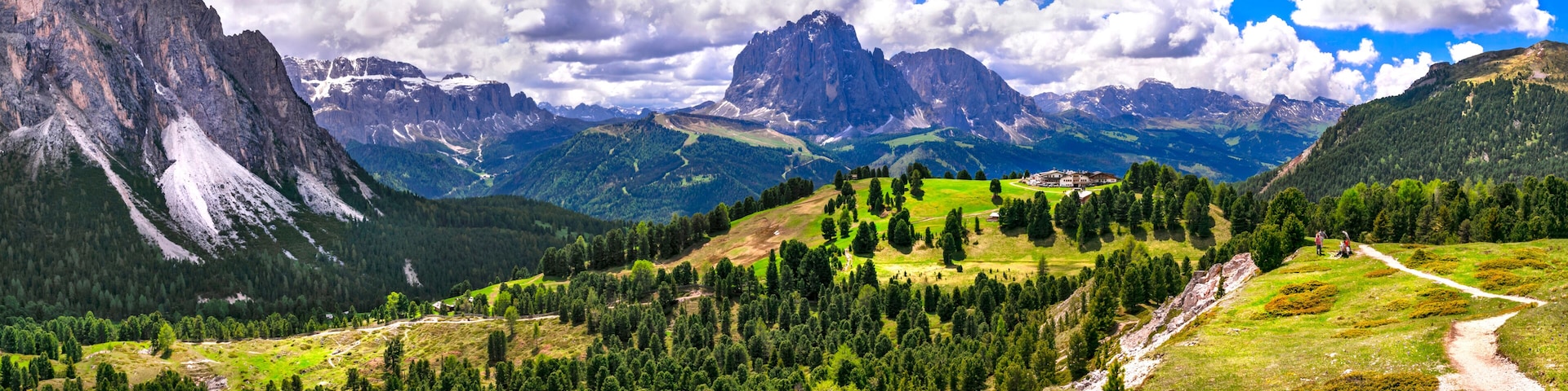 Paisagem montanhosa com céu claro, trilha sinuosa e um edifício no topo de uma colina.