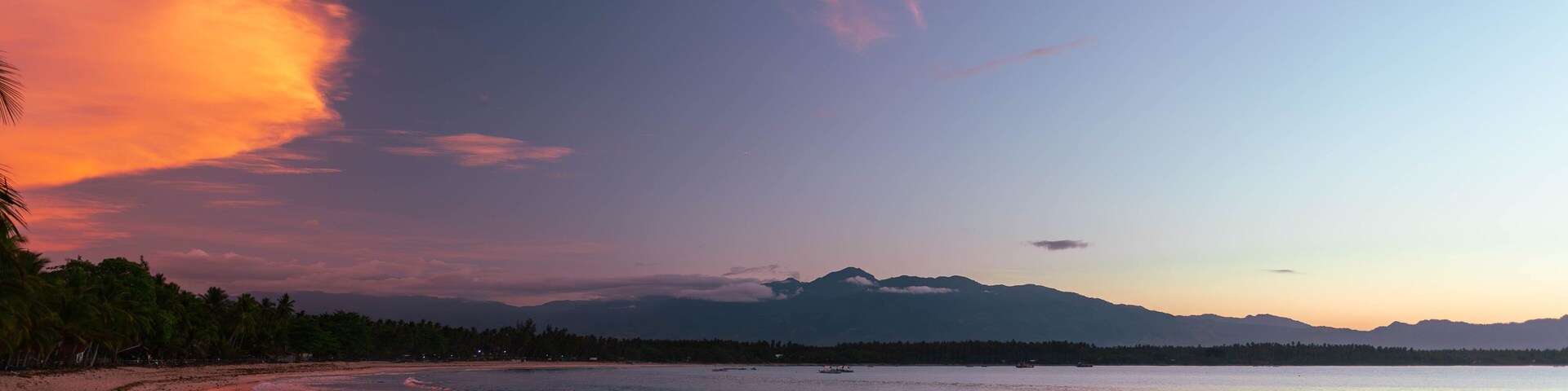 A beach with a curved shoreline, calm water, and a mountain range in the distance.