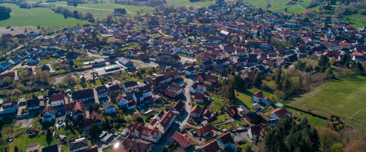 An aerial view of a densely populated village with houses, roads, and surrounding green fields and hills.