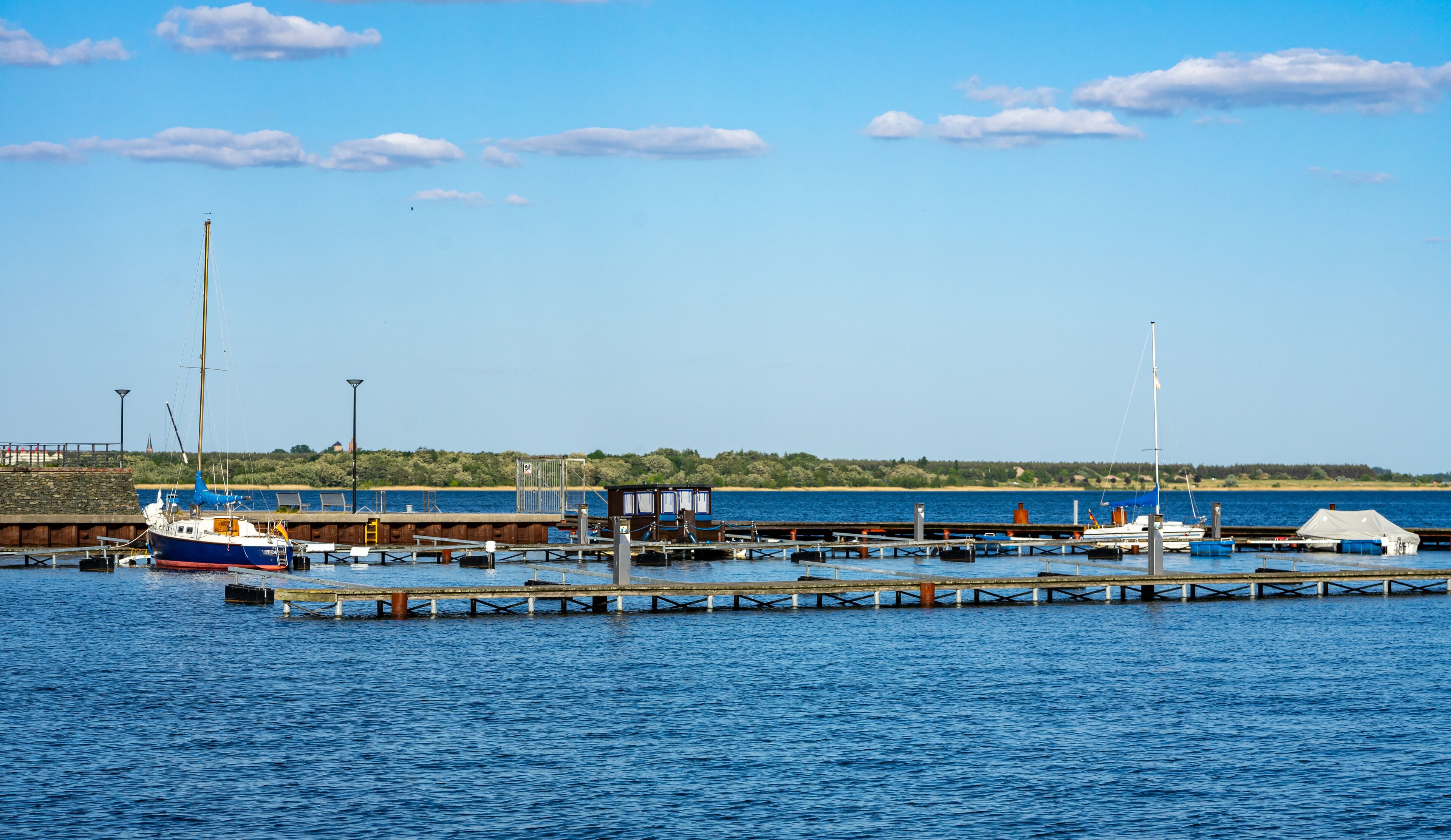 A harbor with boats docked at piers, a lighthouse, and a distant hill with vegetation.