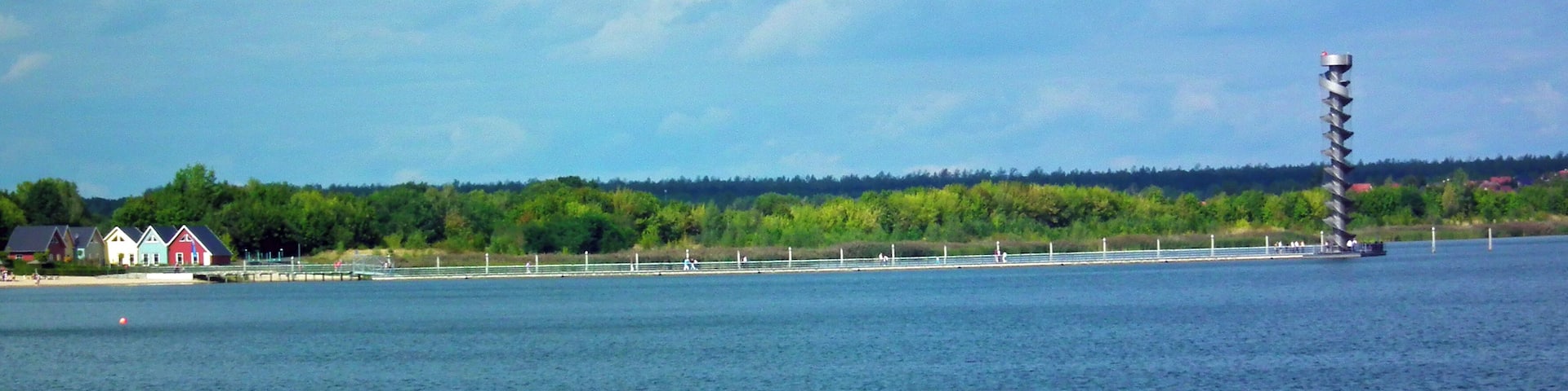 A waterfront with a tall tower, a pier, and colorful buildings along the shore.