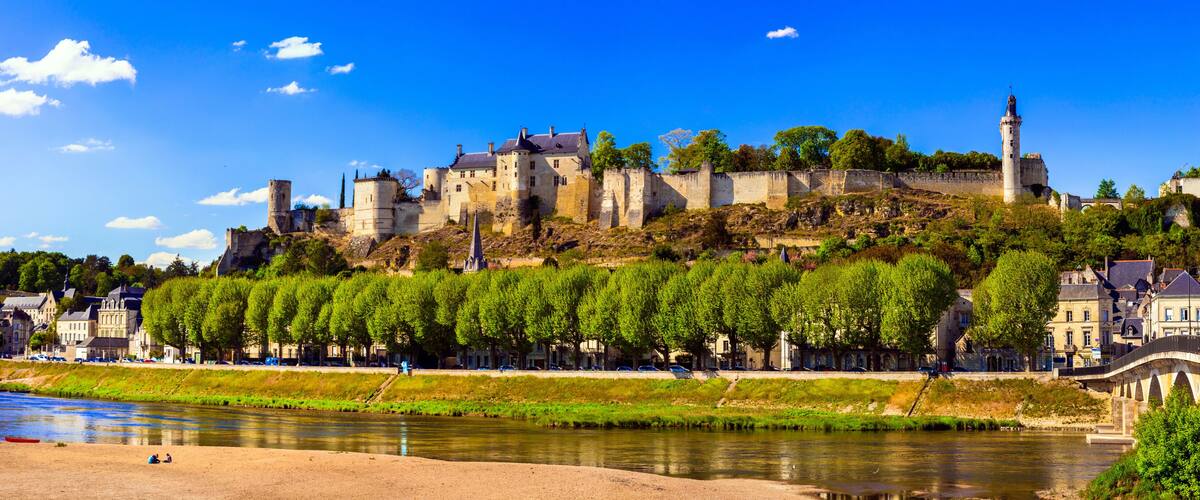 A historic castle on a hill overlooking a river, with a bridge connecting to a town below.