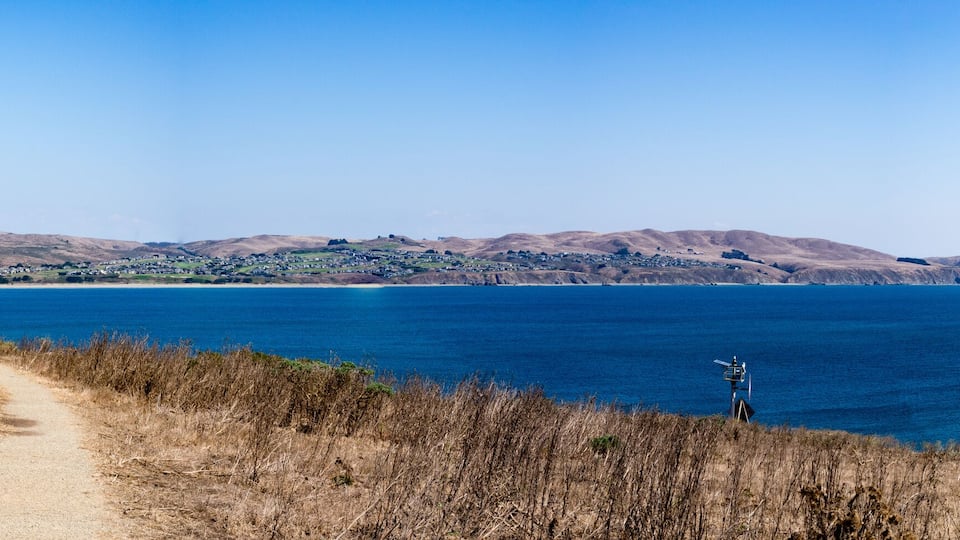 A coastal landscape with a dirt path leading to a lighthouse on a hill overlooking the ocean.