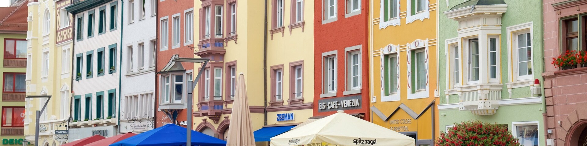 A colorful street with cafes and shops, a sign for 'spitznagel', and a 'United Colors of Benetton' store.