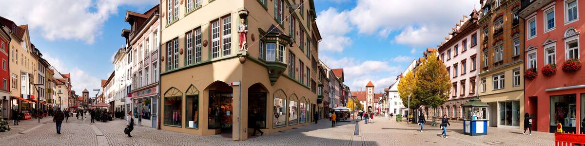 Eine Kopfsteinpflasterstraße gesäumt von bunten, historischen Gebäuden, ein klarer, blauer Himmel und einige Fußgänger.