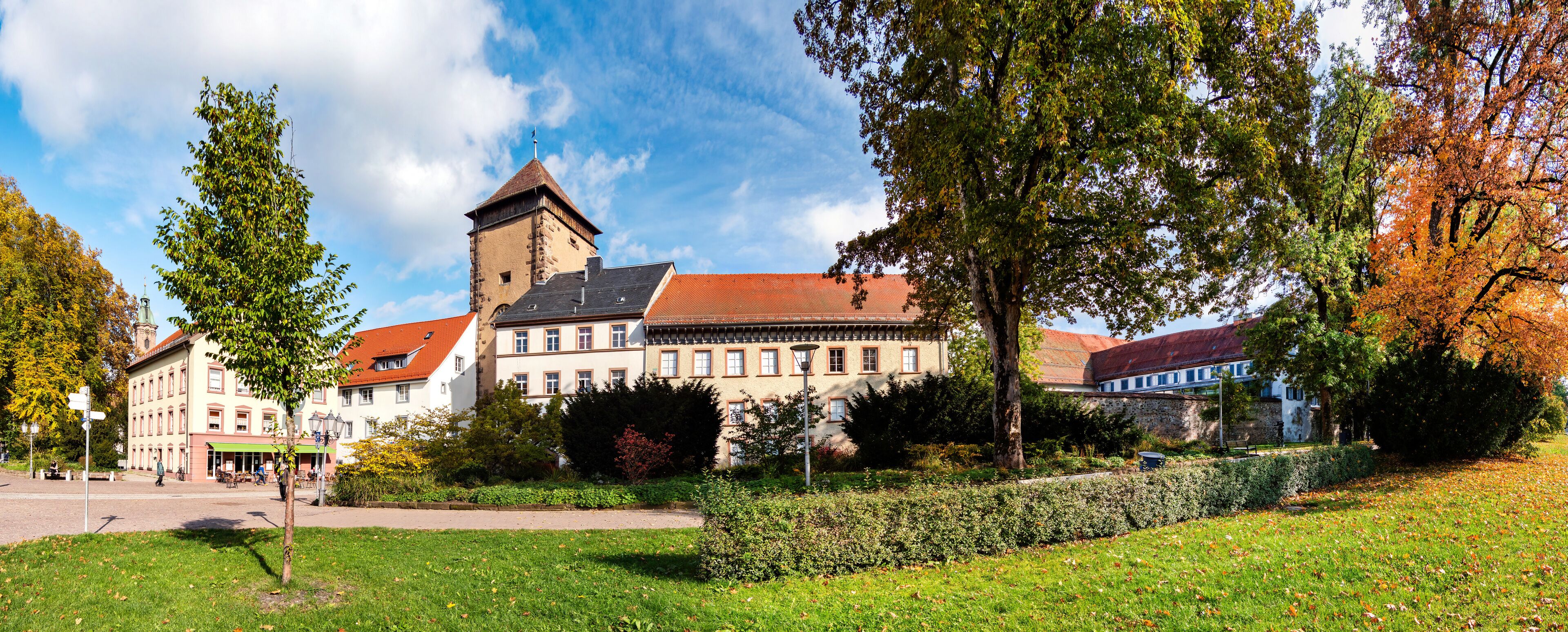 A historic building with a tower, surrounded by trees and a well-maintained lawn.