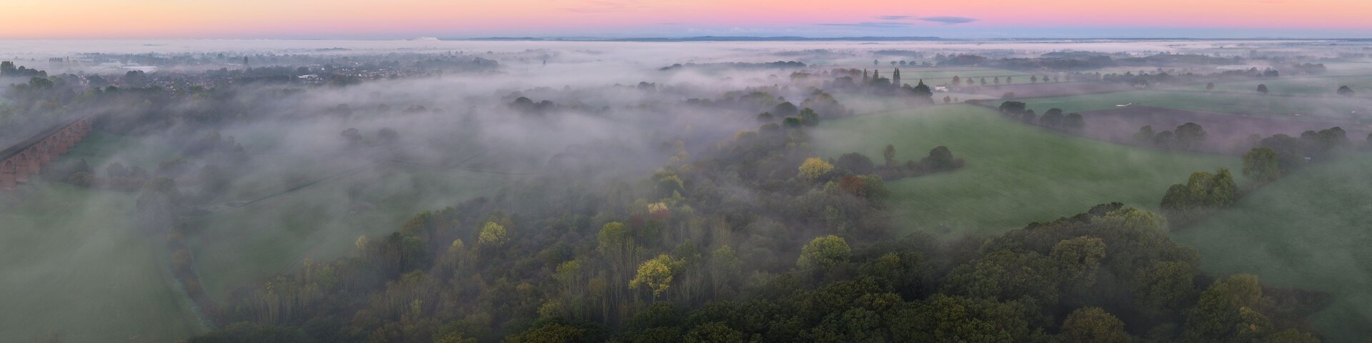 Paisaje brumoso con un puente, densos bosques y un horizonte lejano.