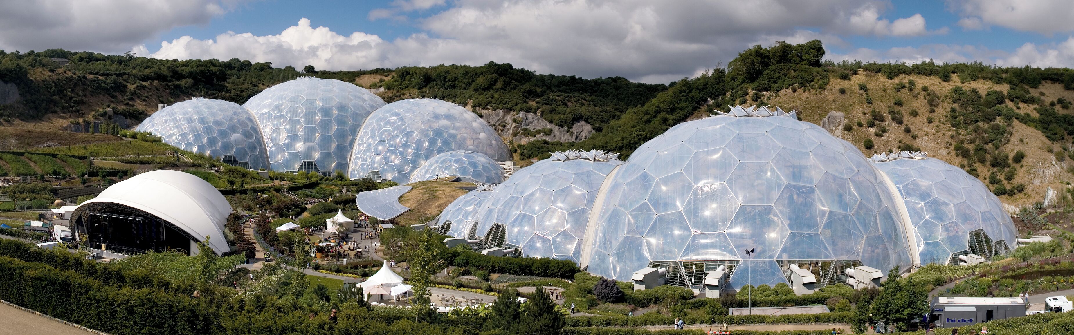 A series of large, transparent geodesic domes in a lush, hilly landscape.