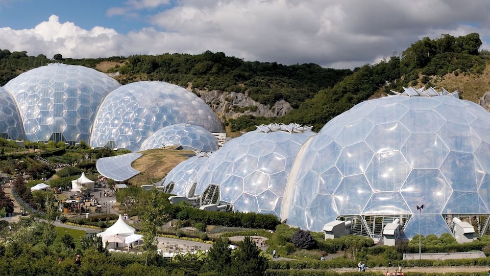 A series of large, transparent geodesic domes in a lush, hilly landscape.