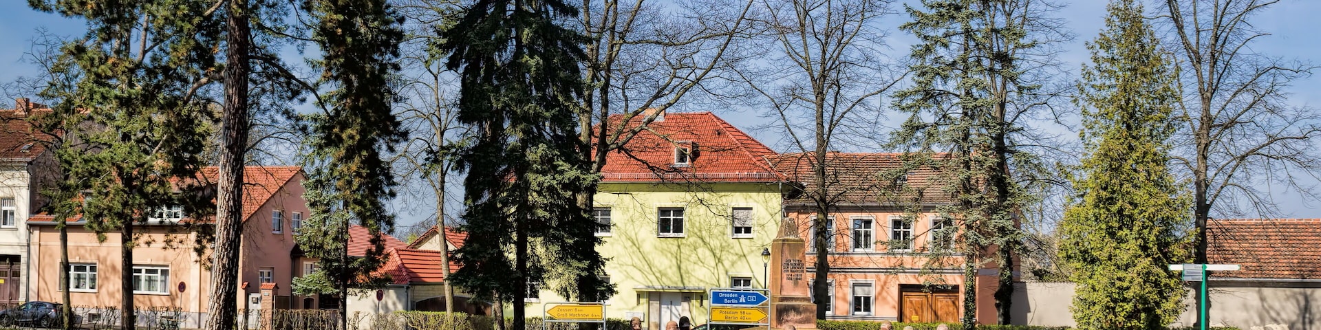 Um parque com um banco, uma lata de lixo e uma fileira de casas com telhados vermelhos.