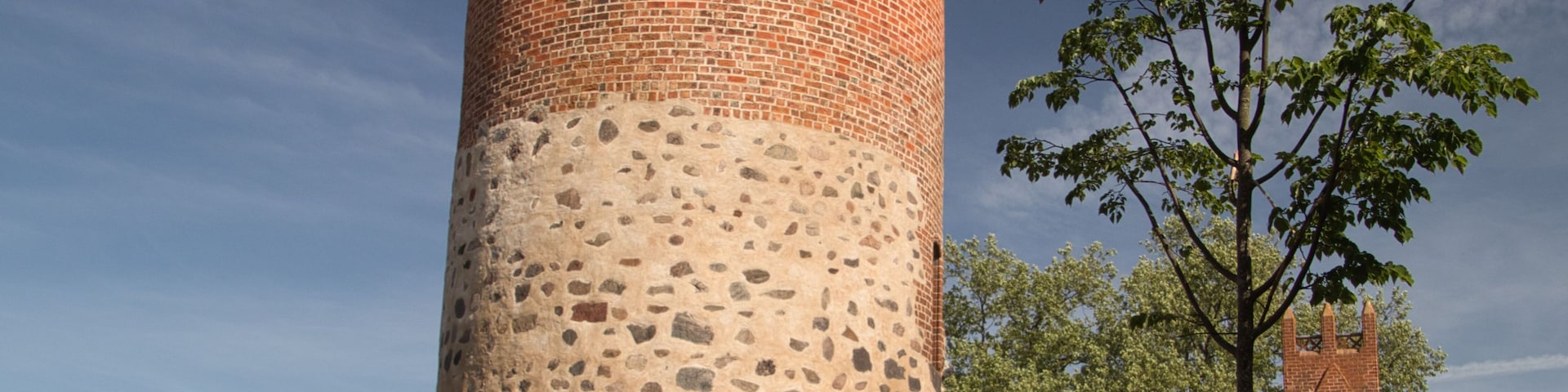 Una torre de ladrillo con almenas, una base de piedra y un árbol al fondo.