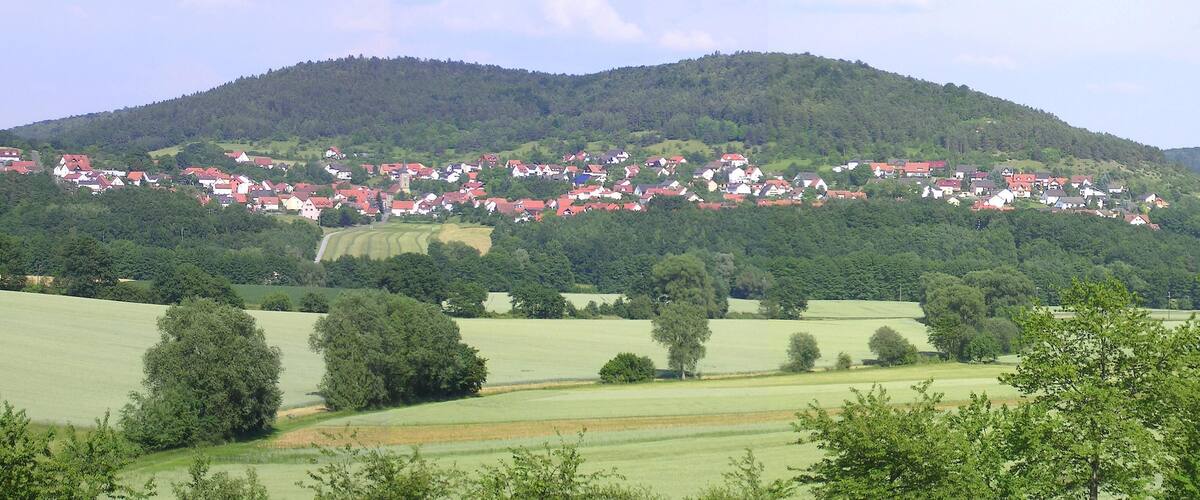 A village nestled in a valley with rolling hills and a church in the background.