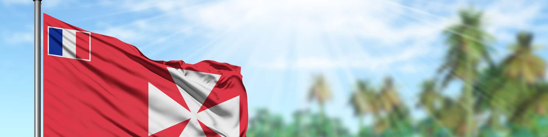 Waving Wallis And Futuna flag in the sunny blue sky with summer beach background. Vacation theme, holiday concept.