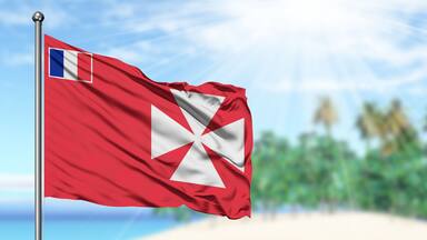 Waving Wallis And Futuna flag in the sunny blue sky with summer beach background. Vacation theme, holiday concept.