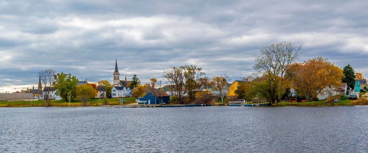 A calm lake with a church and houses in the background.