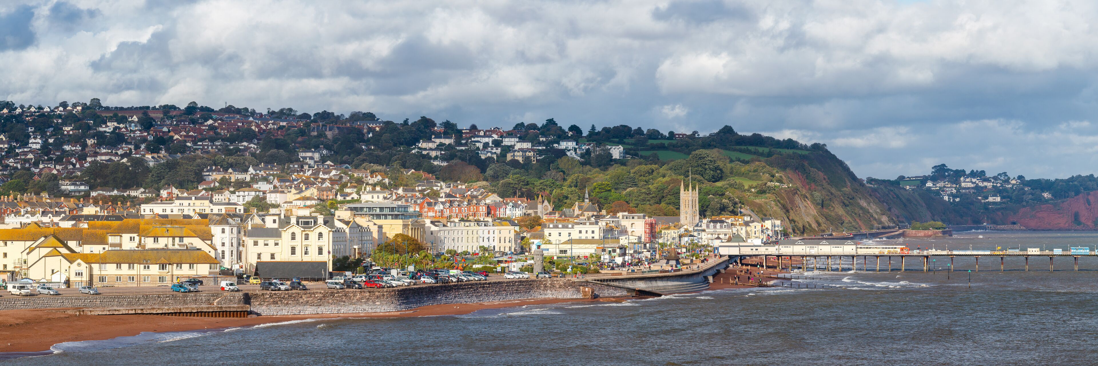 A coastal town with a prominent pier, a historic church, and a hillside with residential buildings.