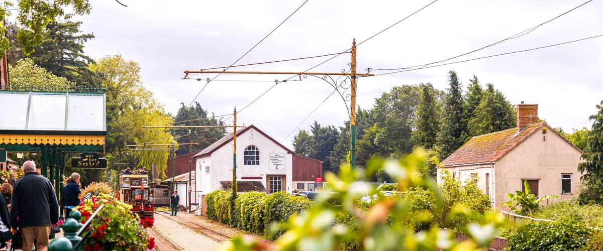 A quaint village street with a tram, vintage buildings, and lush greenery.