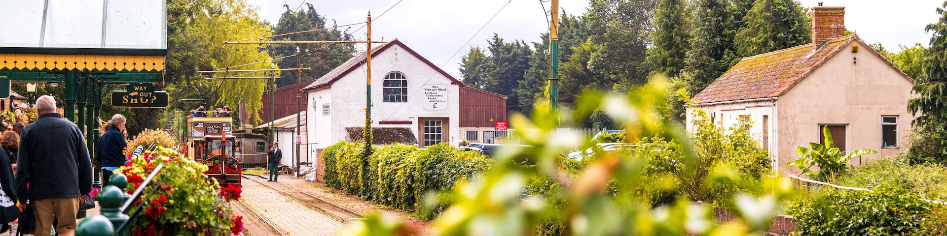 A quaint village street with a tram, vintage buildings, and lush greenery.
