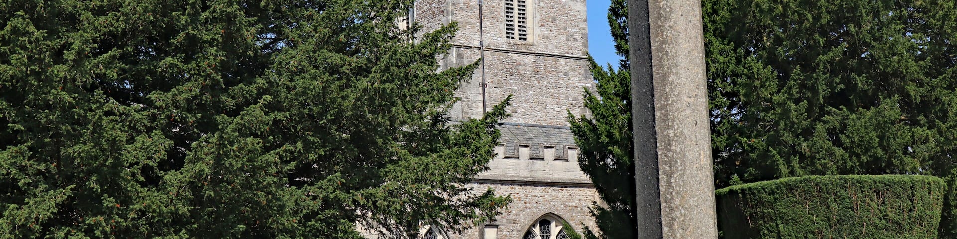 A historic stone tower with intricate architecture, surrounded by lush green trees.