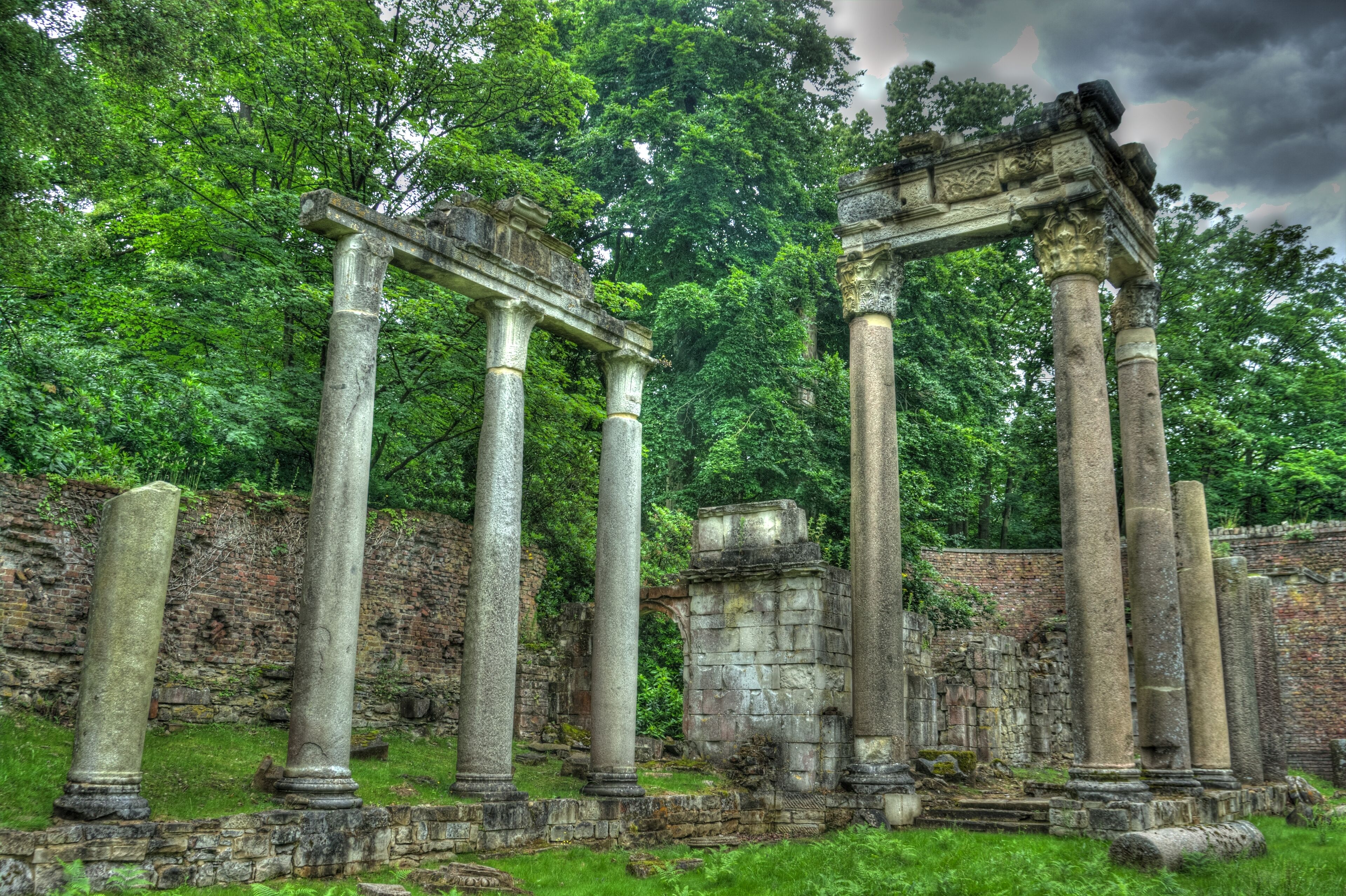 Ancient stone columns and a partially intact archway amidst lush greenery.