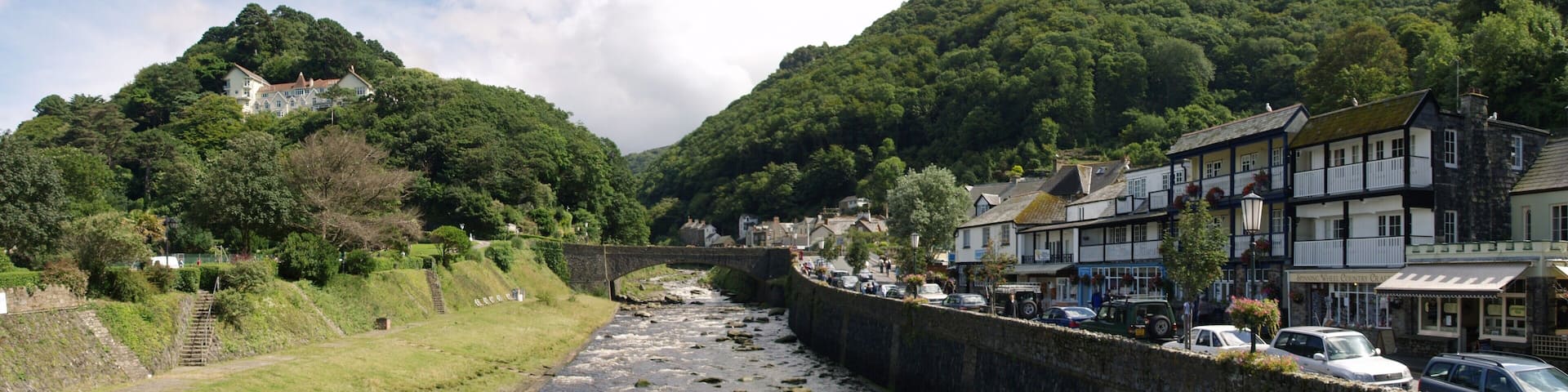 A river flowing through a town with buildings on the right and a bridge in the middle.