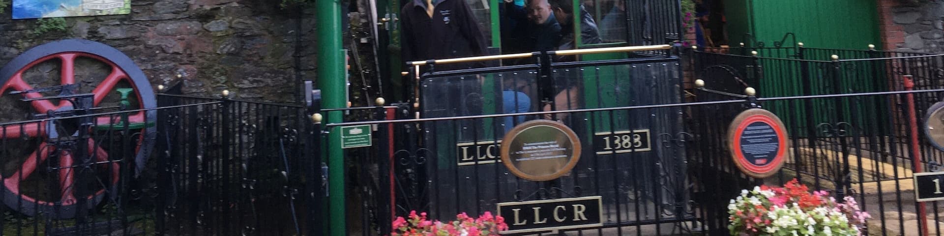 A vintage tram with a green roof, a bell, and a sign reading "LLCR" at a station.