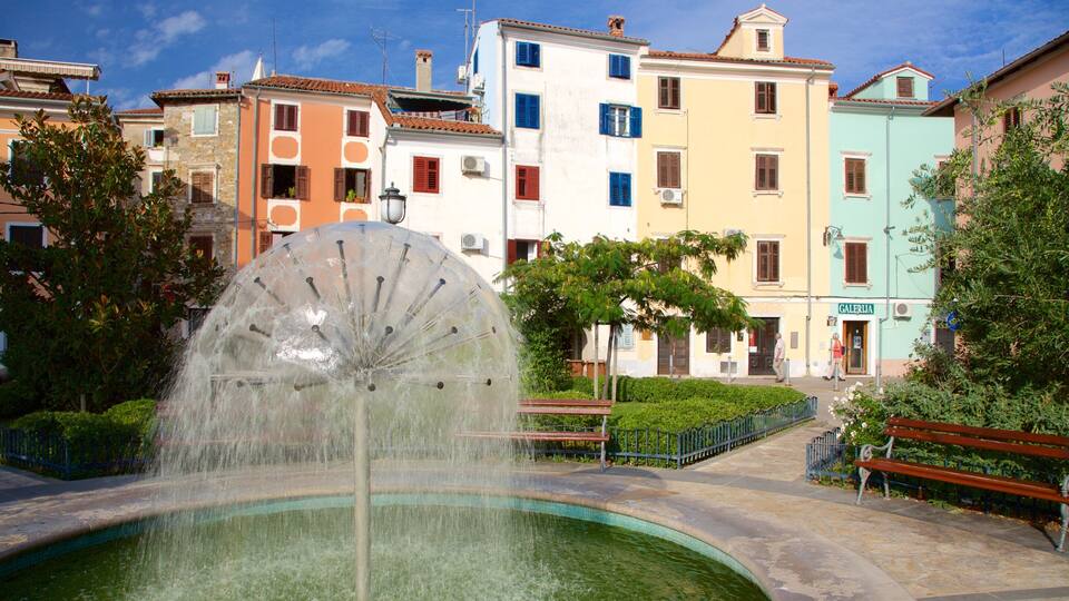 A fountain with a large circular water feature in a public square surrounded by colorful buildings.