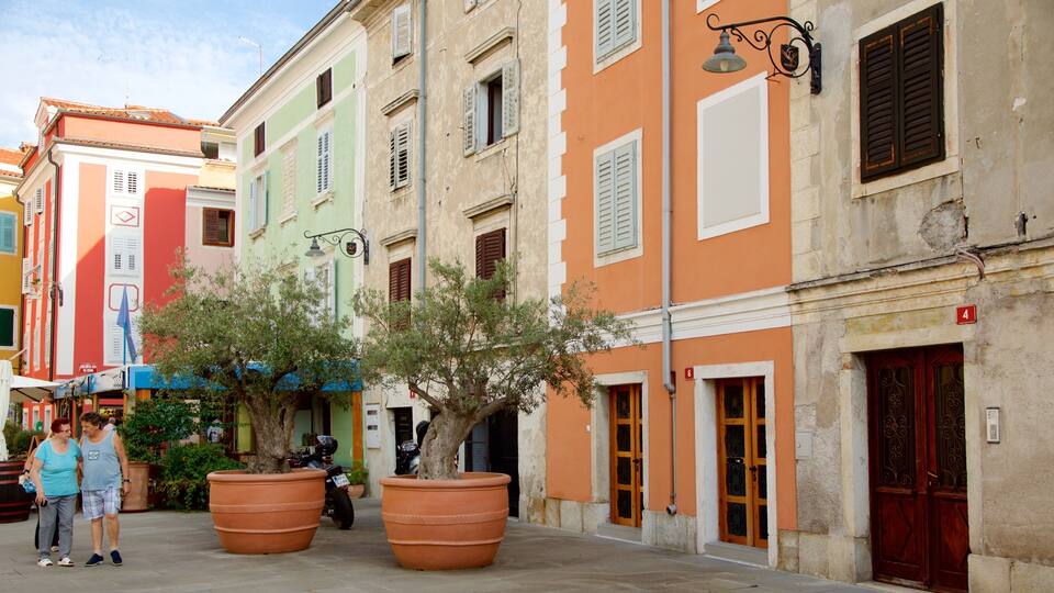 A street with colorful buildings, large terracotta planters, and a tree.