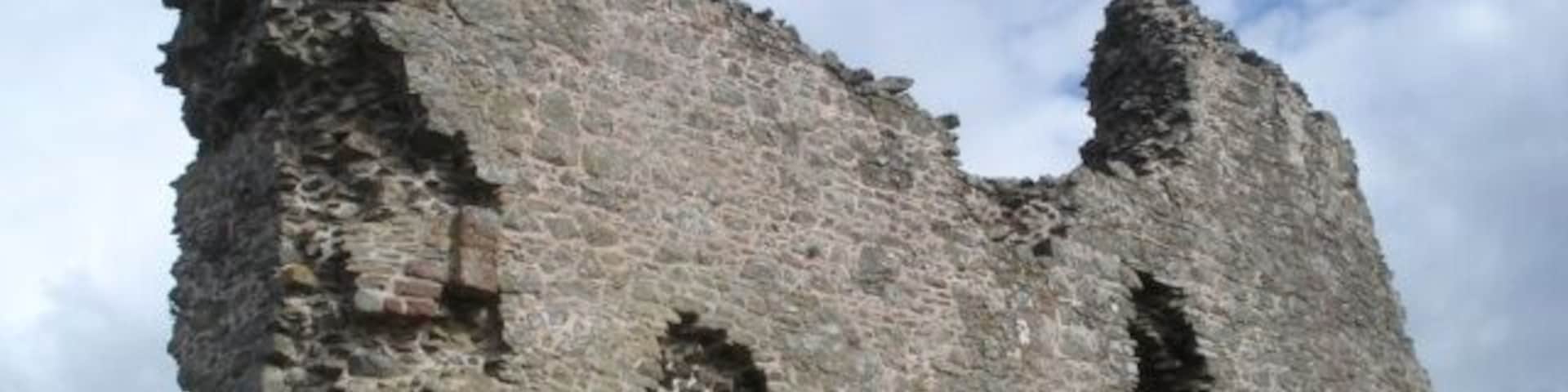 Una torre de piedra alta y deteriorada, con aberturas en arco.