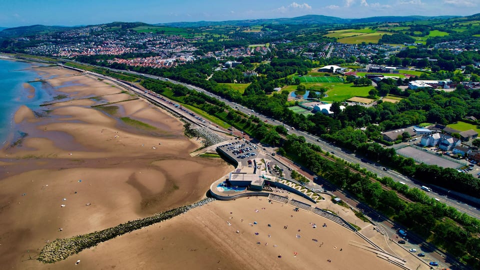 A coastal town with a beach, a parking lot, and a green park area.