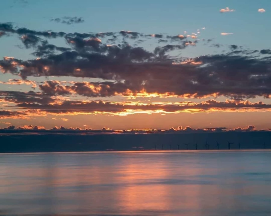 A sunset over a calm body of water with wind turbines in the distance.