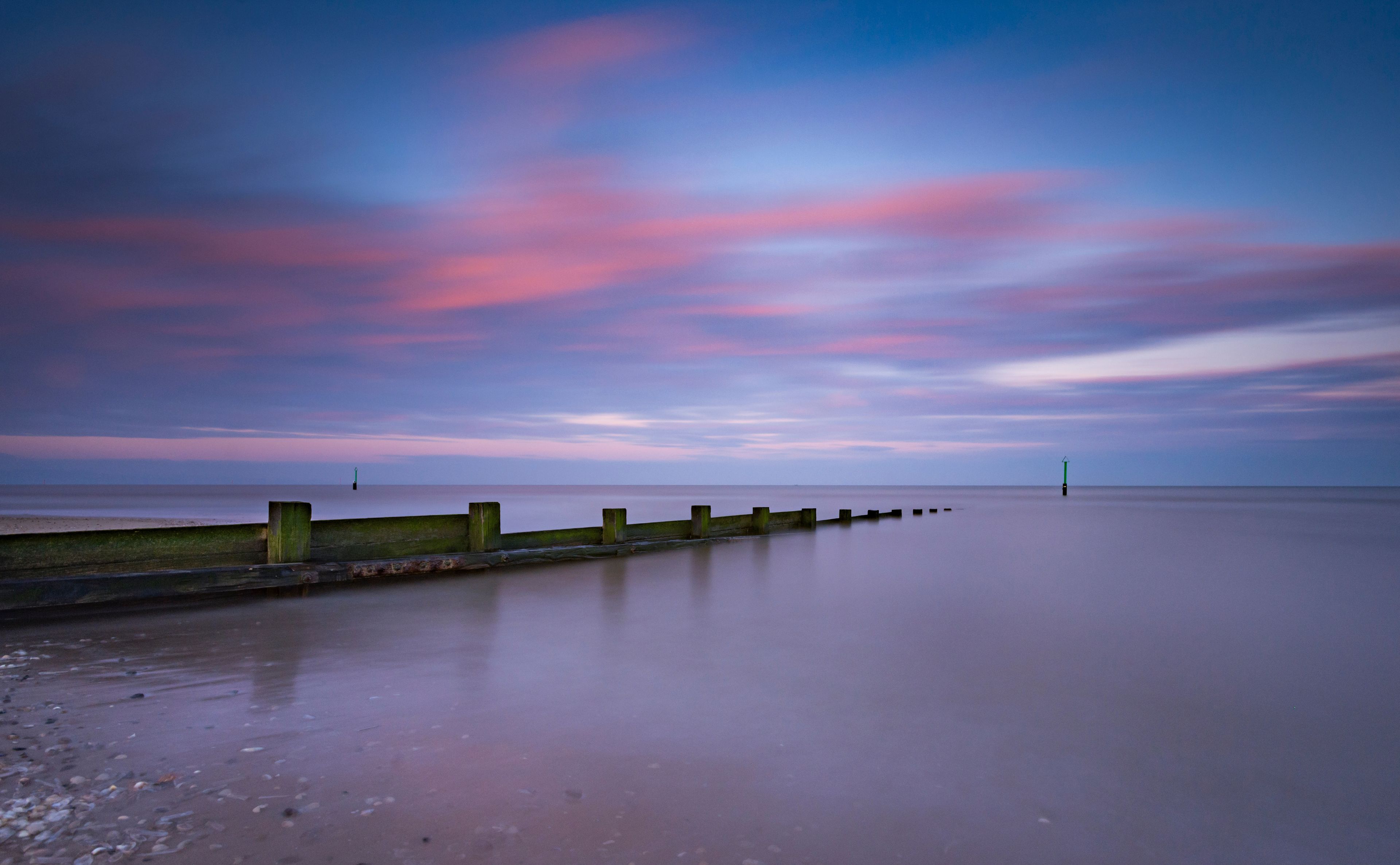 A calm sea with a wooden breakwater and a lighthouse in the distance.