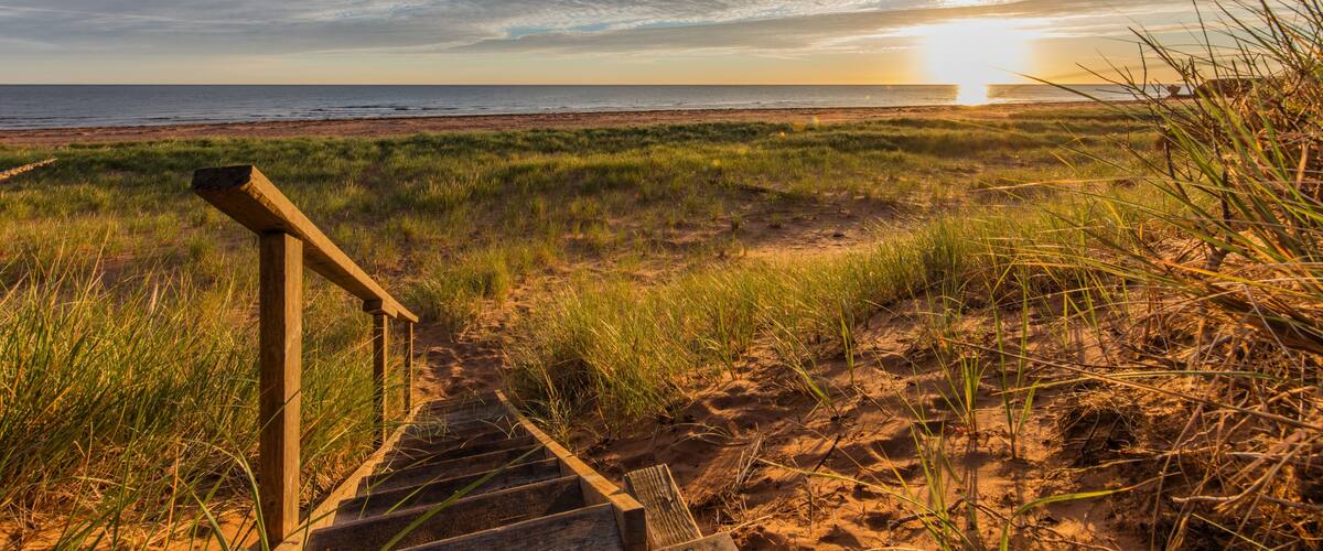A wooden staircase leading to a beach with a sunset in the background.