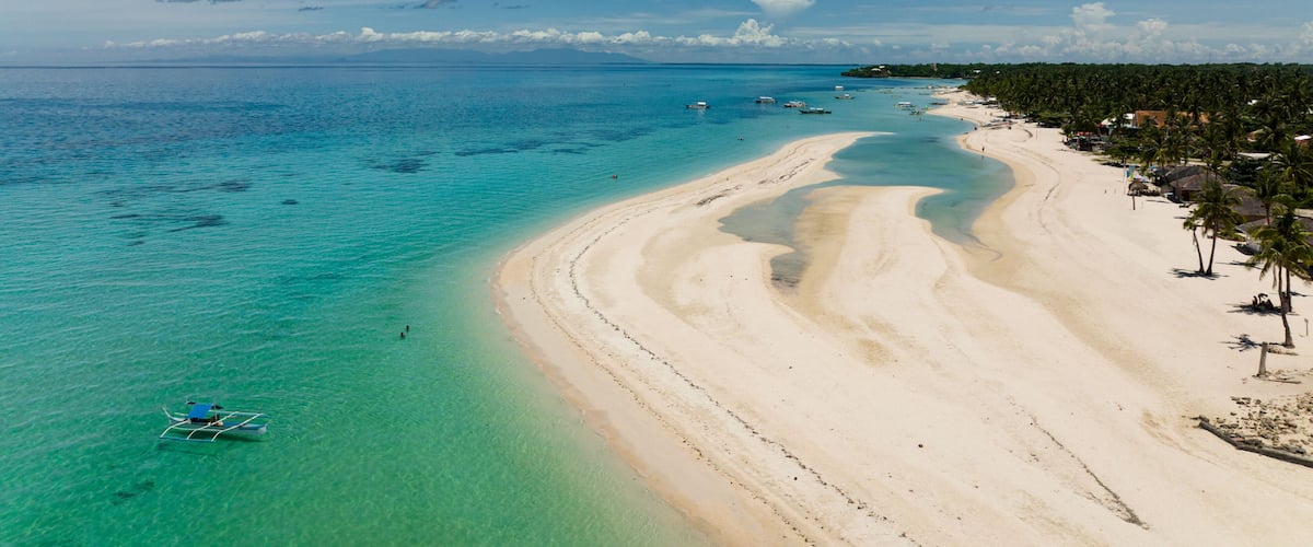 A tropical beach with clear turquoise waters, a sandy shoreline, and a row of palm trees.
