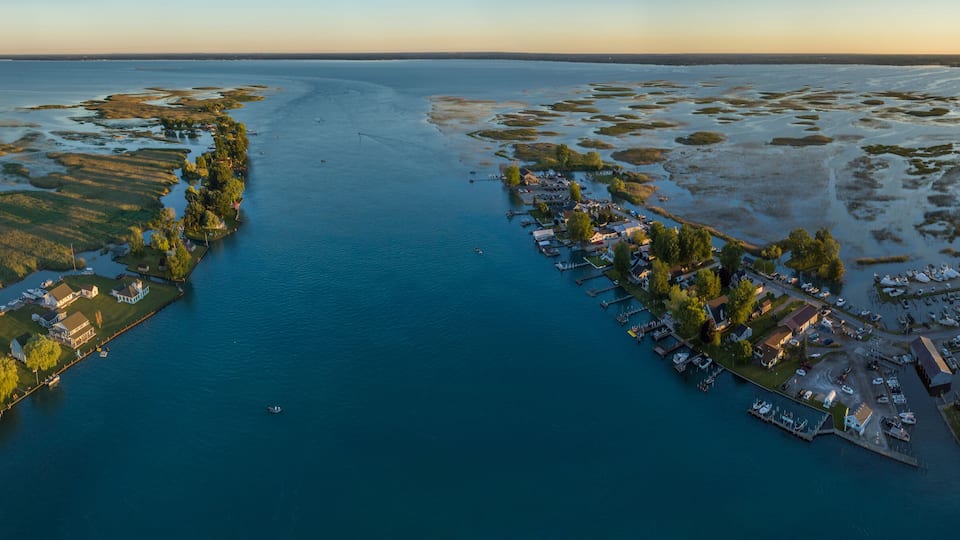 An aerial view of a coastal town with a marina, houses, and a large body of water.
