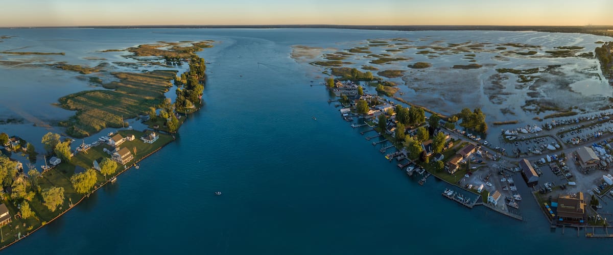 An aerial view of a coastal town with a marina, houses, and a large body of water.