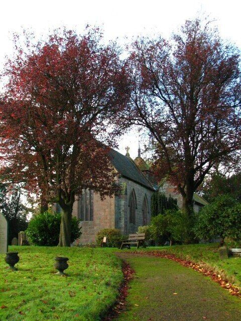 A church with a stone facade, surrounded by a well-maintained lawn and trees with autumn leaves.