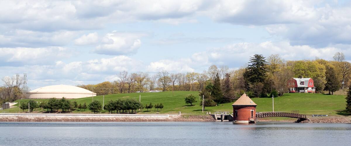 A lake with a red tower, a white dome structure, and a red house on a hill.