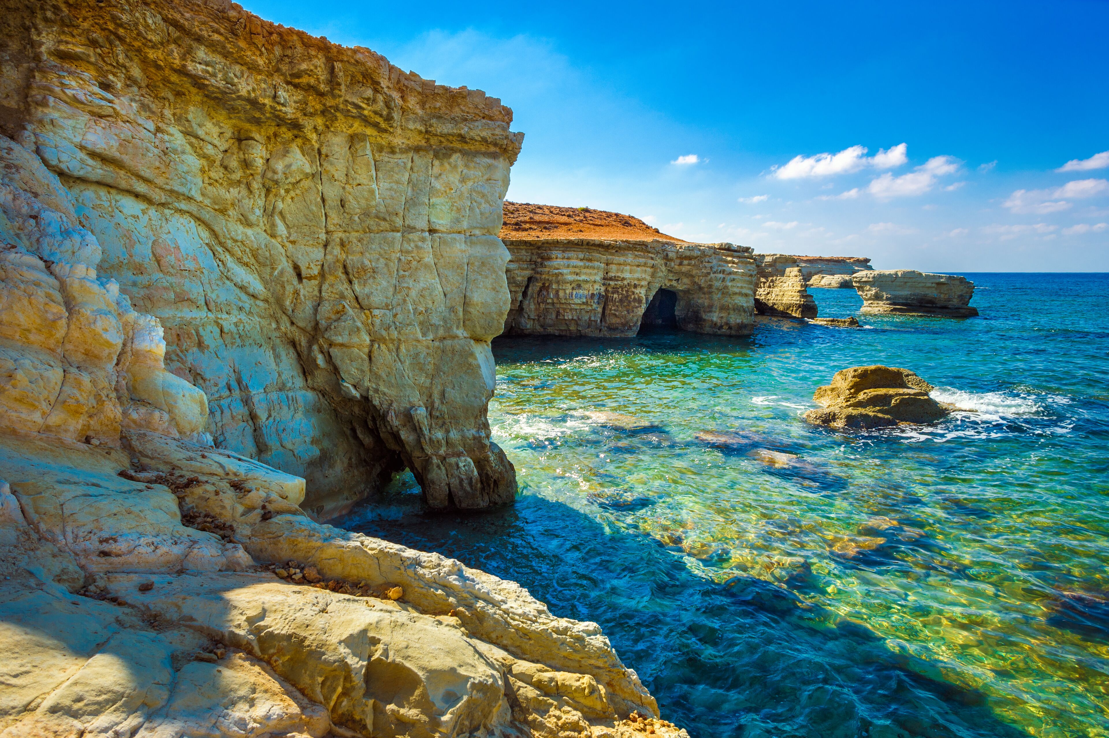 A coastal cliff with clear blue waters and a rocky outcrop.