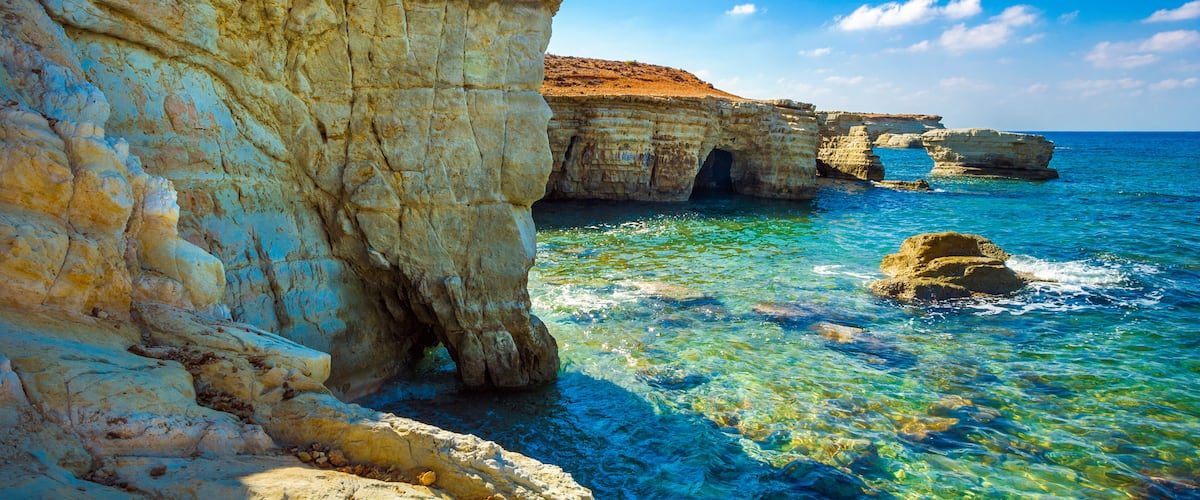 A coastal cliff with clear blue waters and a rocky outcrop.
