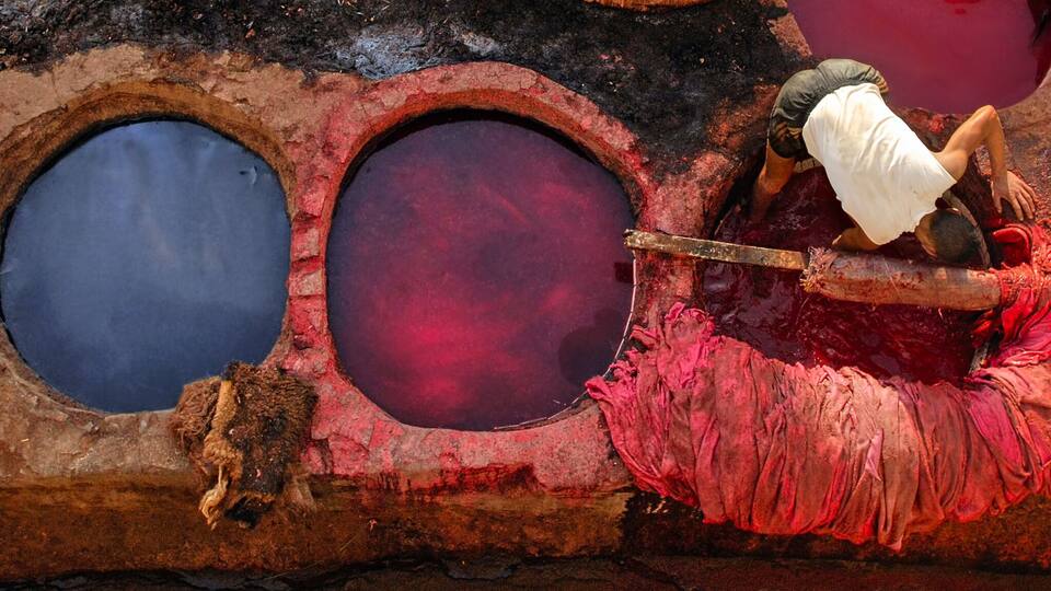 A traditional dyeing setup with multiple vats of red and blue dye.