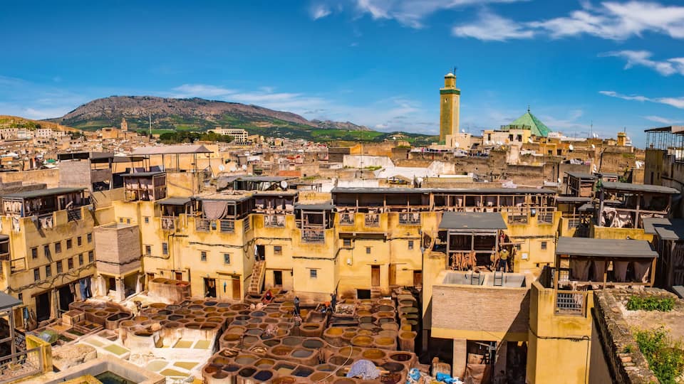 A historic town with terracotta-roof buildings, a prominent minaret, and a hillside in the background.