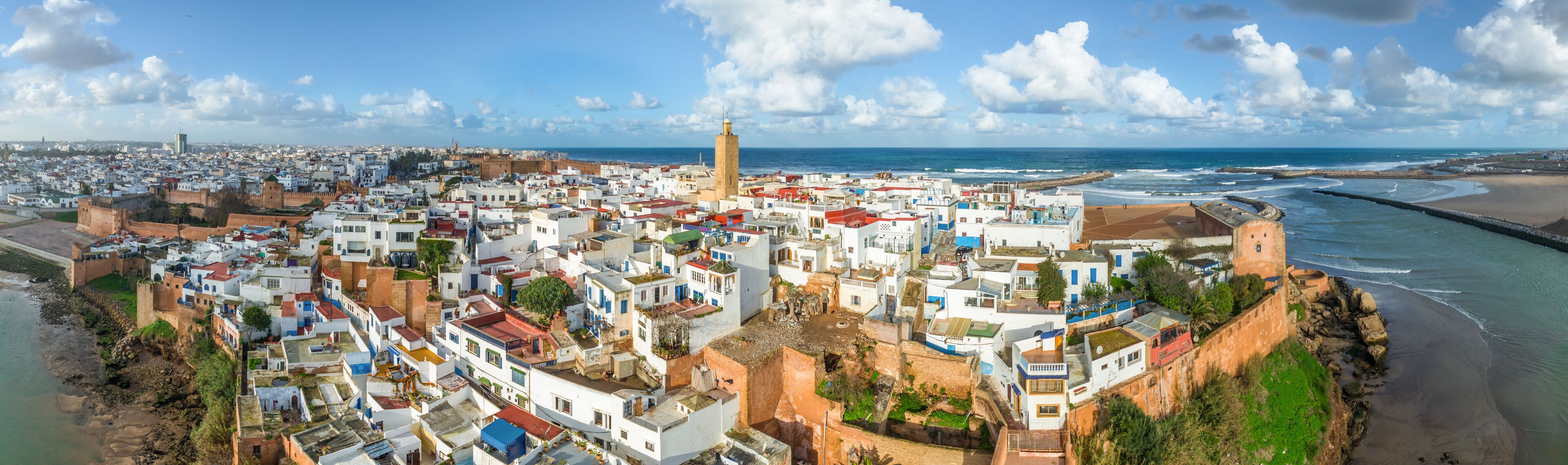 Un paysage urbain côtier avec des bâtiments blancs, une tour imposante et une plage.