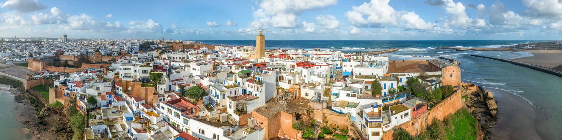 Un paysage urbain côtier avec des bâtiments blancs, une tour imposante et une plage.
