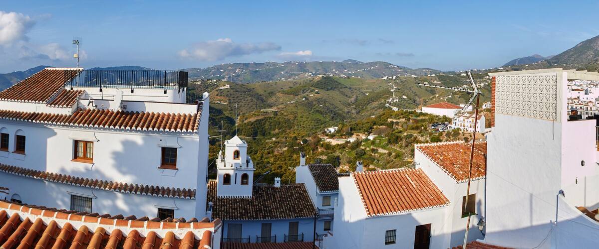 A coastal town with terracotta-tiled rooftops, white buildings, and a mountainous backdrop.