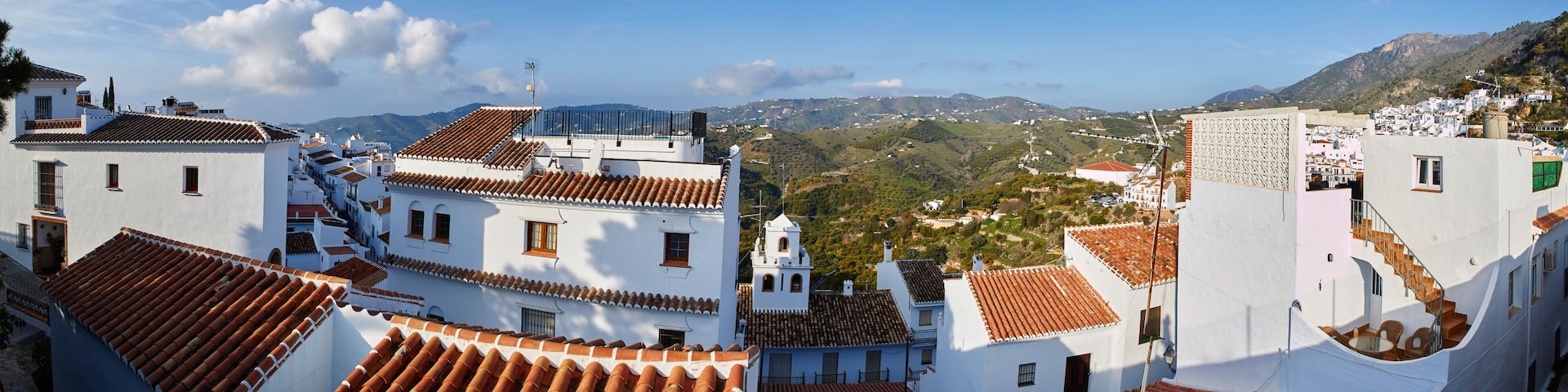 A coastal town with terracotta-tiled rooftops, white buildings, and a mountainous backdrop.