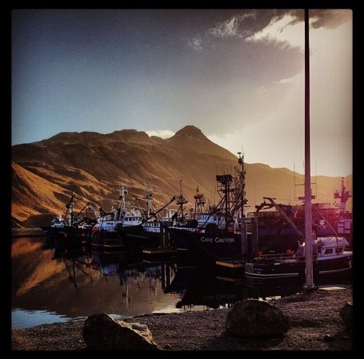A harbor with boats docked, a mountain in the background, and a clear sky.